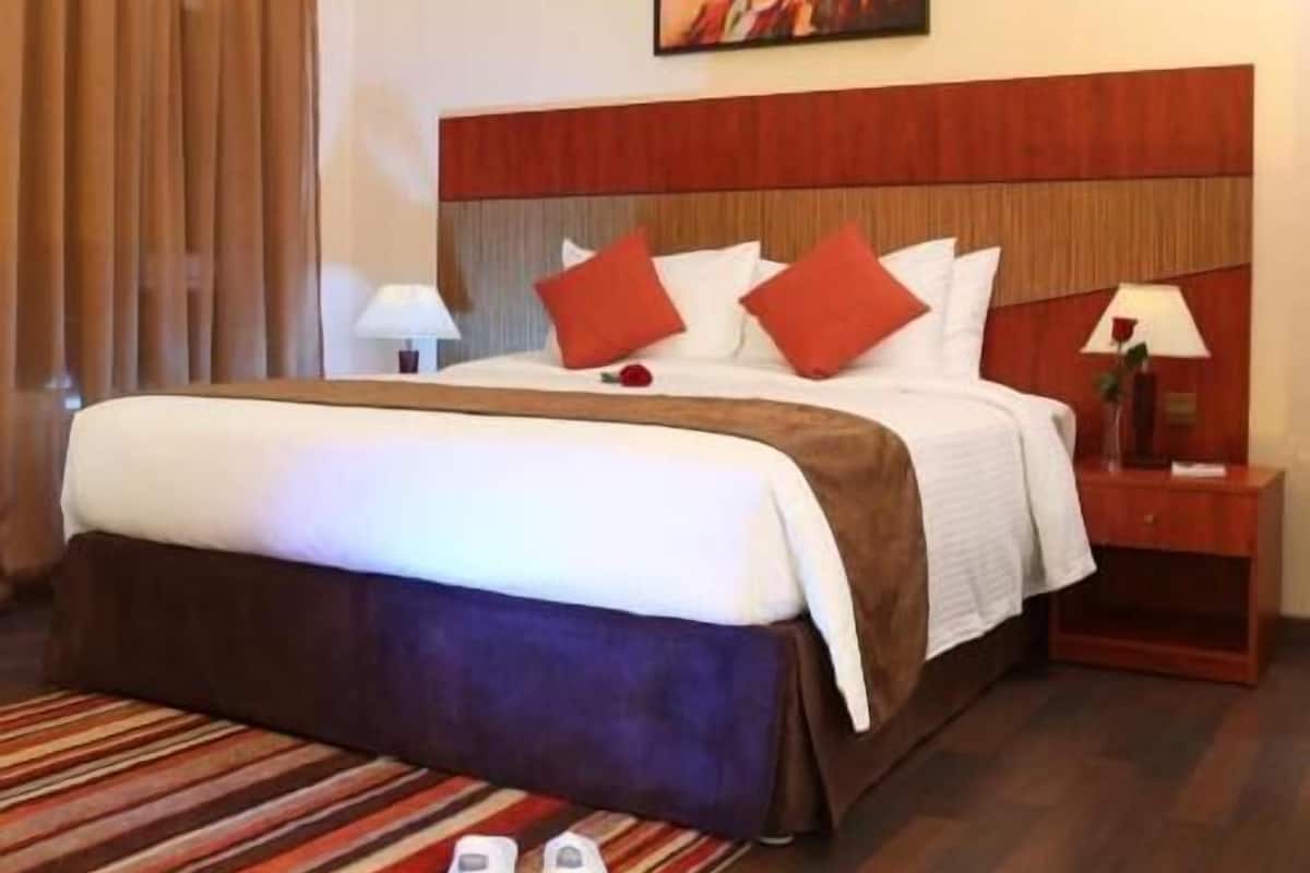 A hotel room with a bed, a nightstand, a lamp, and a pair of slippers on the floor.