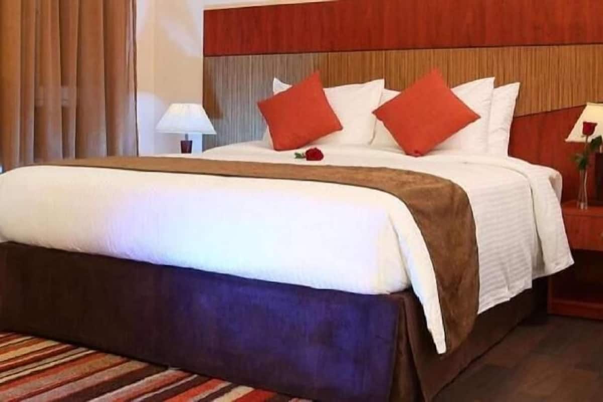A hotel room with a bed, a nightstand, a lamp, and a window with curtains.
