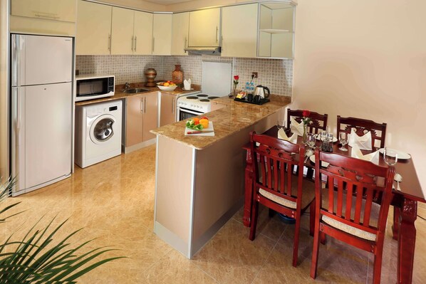 Una cocina compacta con lavadora integrada, microondas y estufa. Hay un comedor con sillas de madera y una mesa.