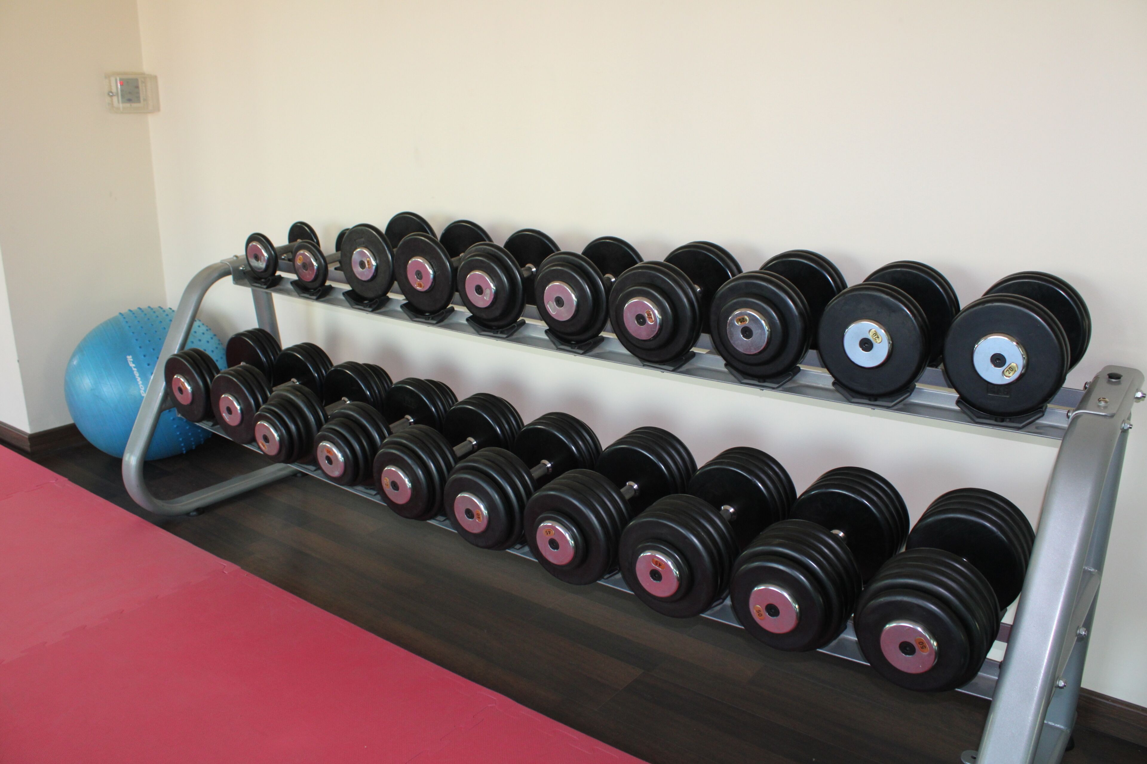 Un gimnasio con un estante de mancuernas y una pelota de ejercicios azul.