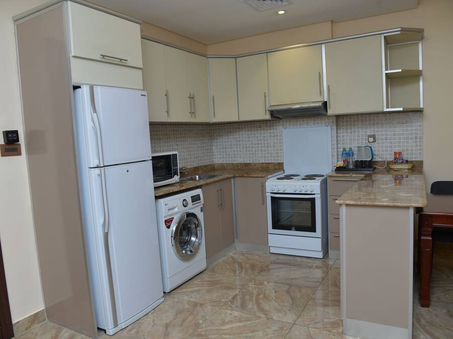 A compact kitchen with a refrigerator, washing machine, microwave, stove, and tiled backsplash.