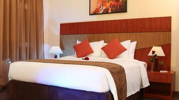A hotel room with a large bed, a wooden headboard, a red and brown striped rug, and a single nightstand with a lamp.