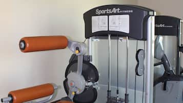 A gym with a weight machine, a television on the wall, and a mirror.