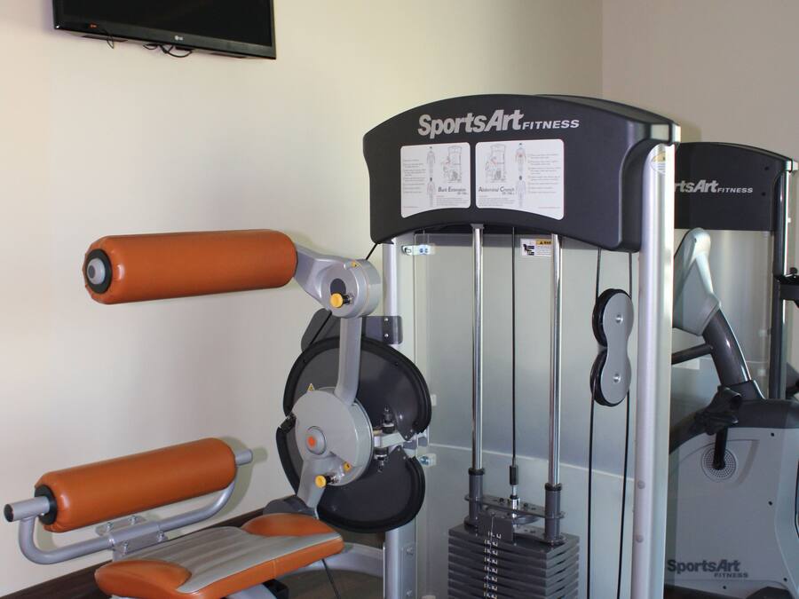 A gym with a weight machine, a television on the wall, and a mirror.