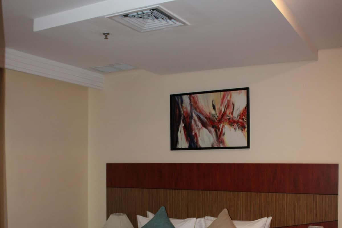 A hotel room with a large bed, two bedside tables, a ceiling light, and a wall-mounted artwork.