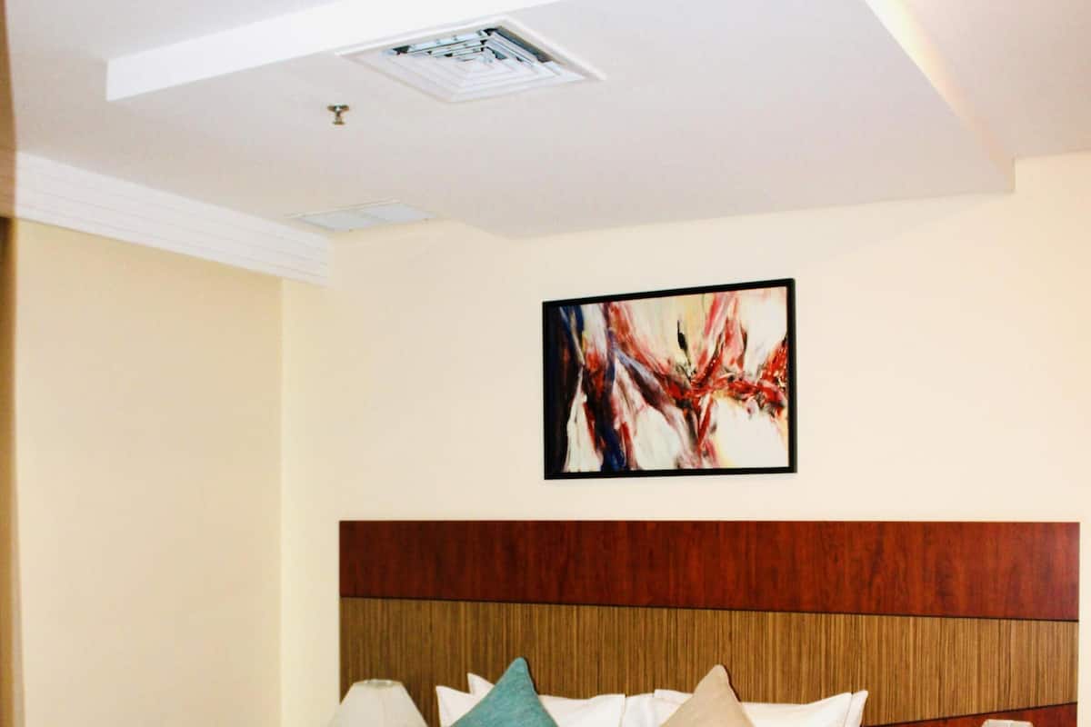 A hotel room with a large bed, wooden headboard, two bedside tables with lamps, and a ceiling light fixture.