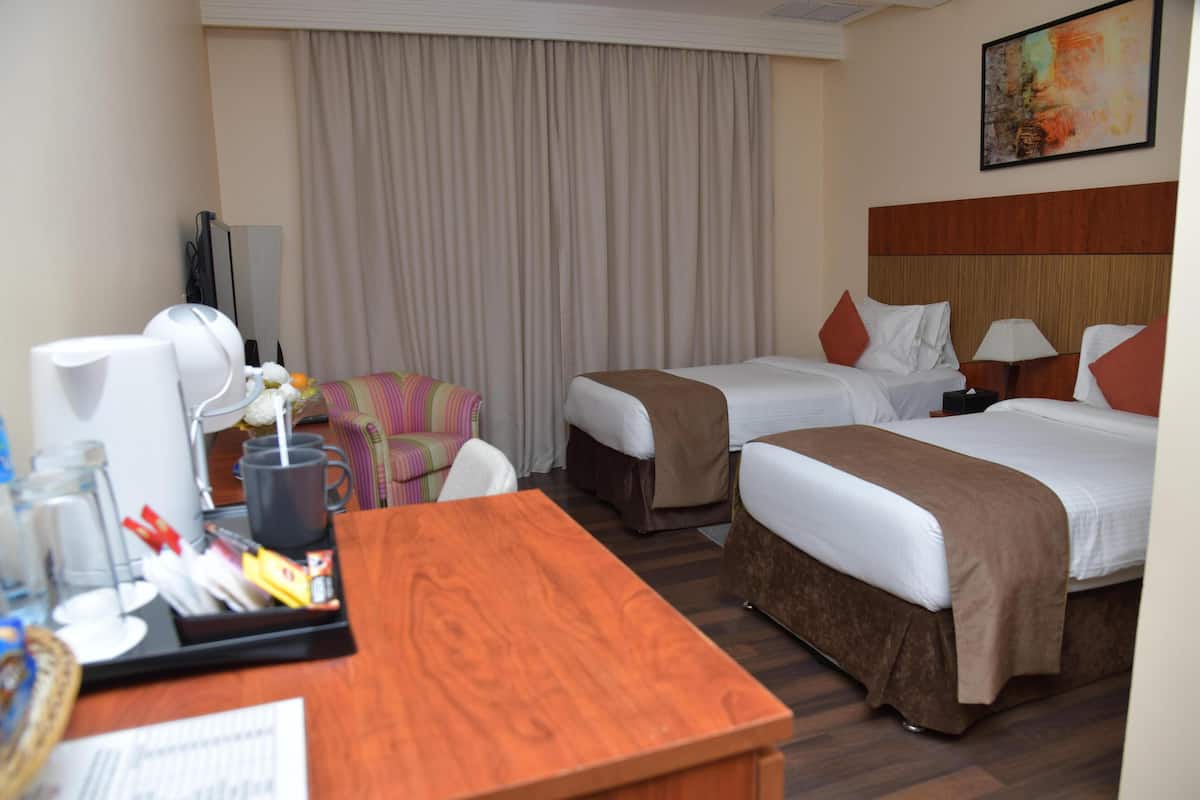 A hotel room with two beds, a desk with a tray of items, a television, and a large window with curtains.