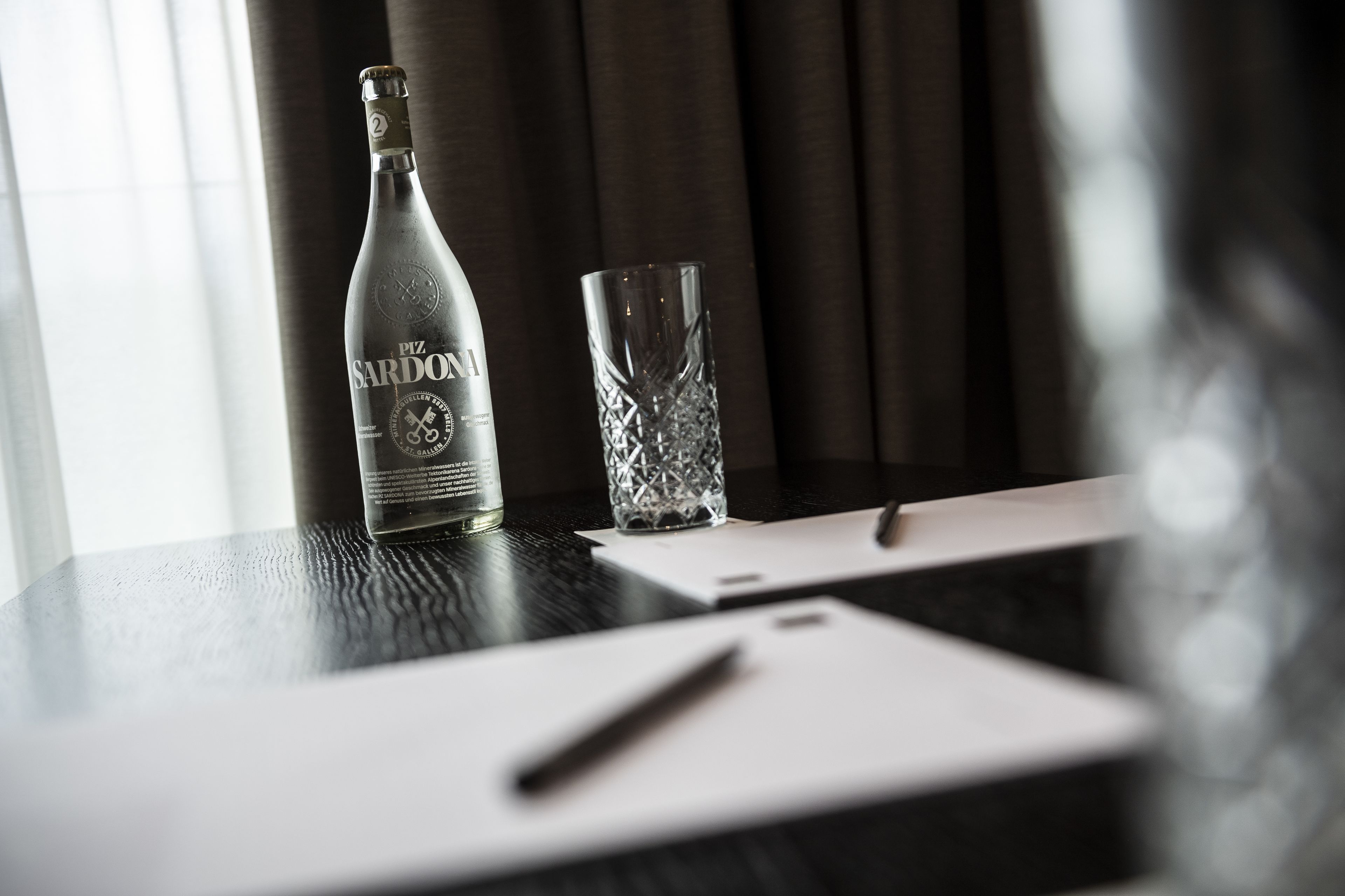 A bottle of Piz Sardo on a table with a glass and a pen.