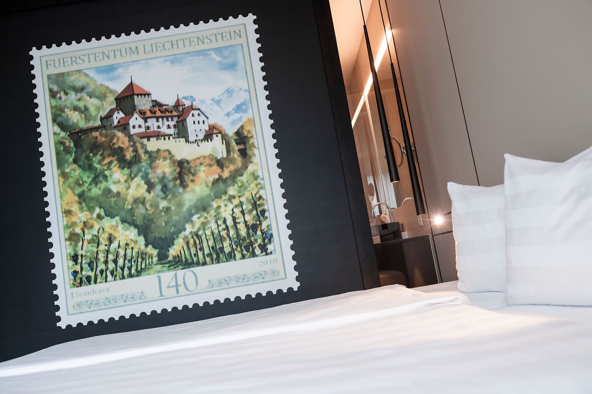 A hotel room with a bed, a wall-mounted poster of a castle, and a modern light fixture.