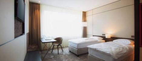 Habitación de hotel con dos camas, un escritorio, una silla y un televisor.