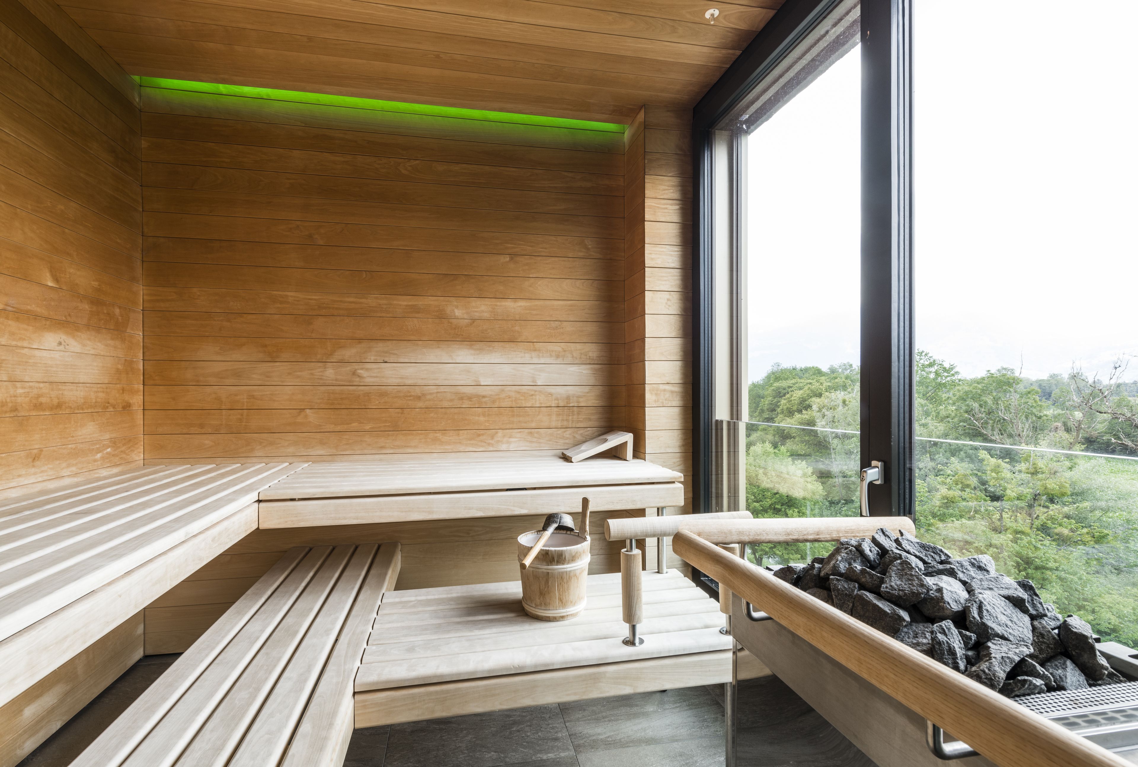 Eine Holzsauna mit Bänken, einem Holztisch, einem Eimer mit Bürste und einem Steinhaufen.