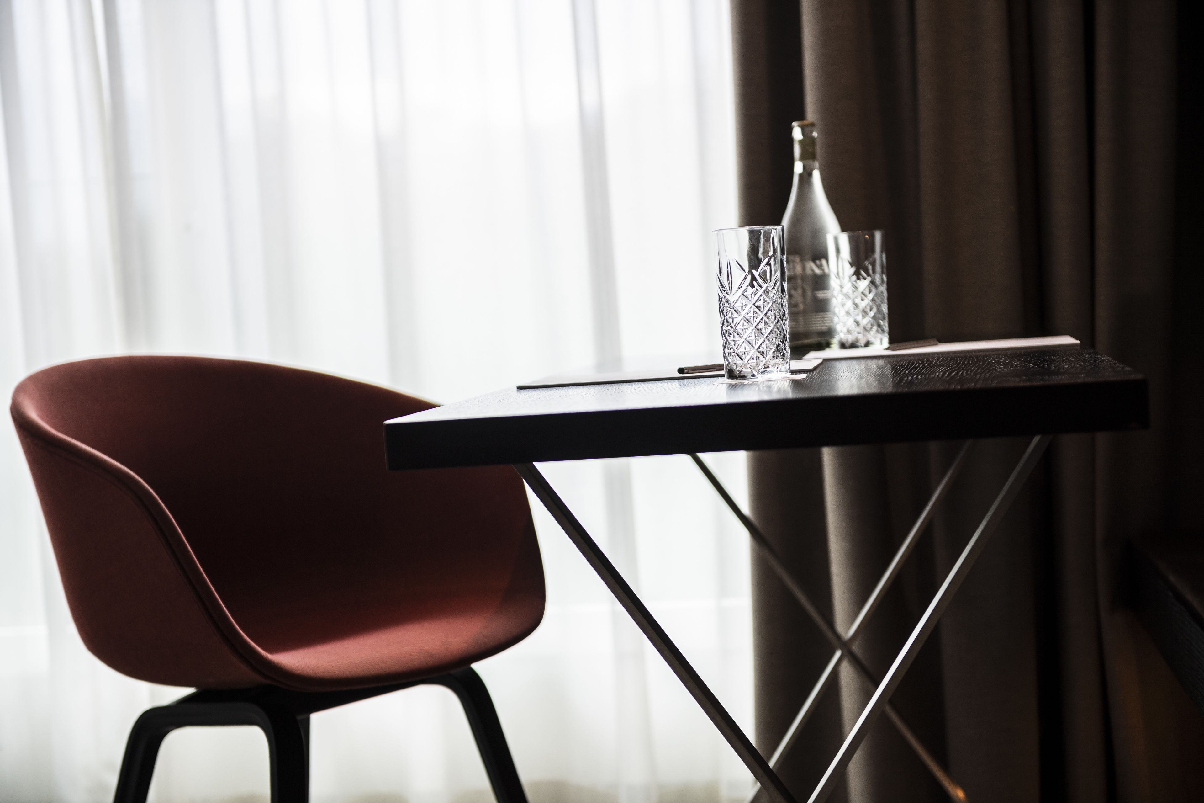 Une pièce moderne avec une table sombre, une chaise rouge, une bouteille et un verre.
