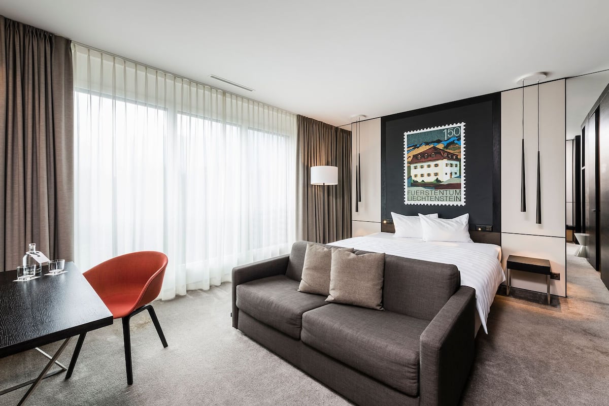 A hotel room with a bed, a sofa, a desk, and a chair.