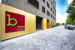 Un edificio con un gran letrero que dice 'b smart' en la fachada, revestimiento de ladrillo y un área de entrada pavimentada.