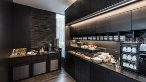 Eine moderne Küche mit dunklen Schränken, einer Wand aus Ziegelsteinen und einer Frühstückstheke mit verschiedenen Lebensmitteln und Küchenutensilien.