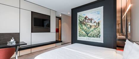 A modern hotel room with a bed, a desk, a TV, and a large poster on the wall.