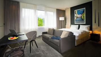 Una habitación de hotel con una cama, un escritorio con una computadora portátil, una silla y vistas a espacios verdes.