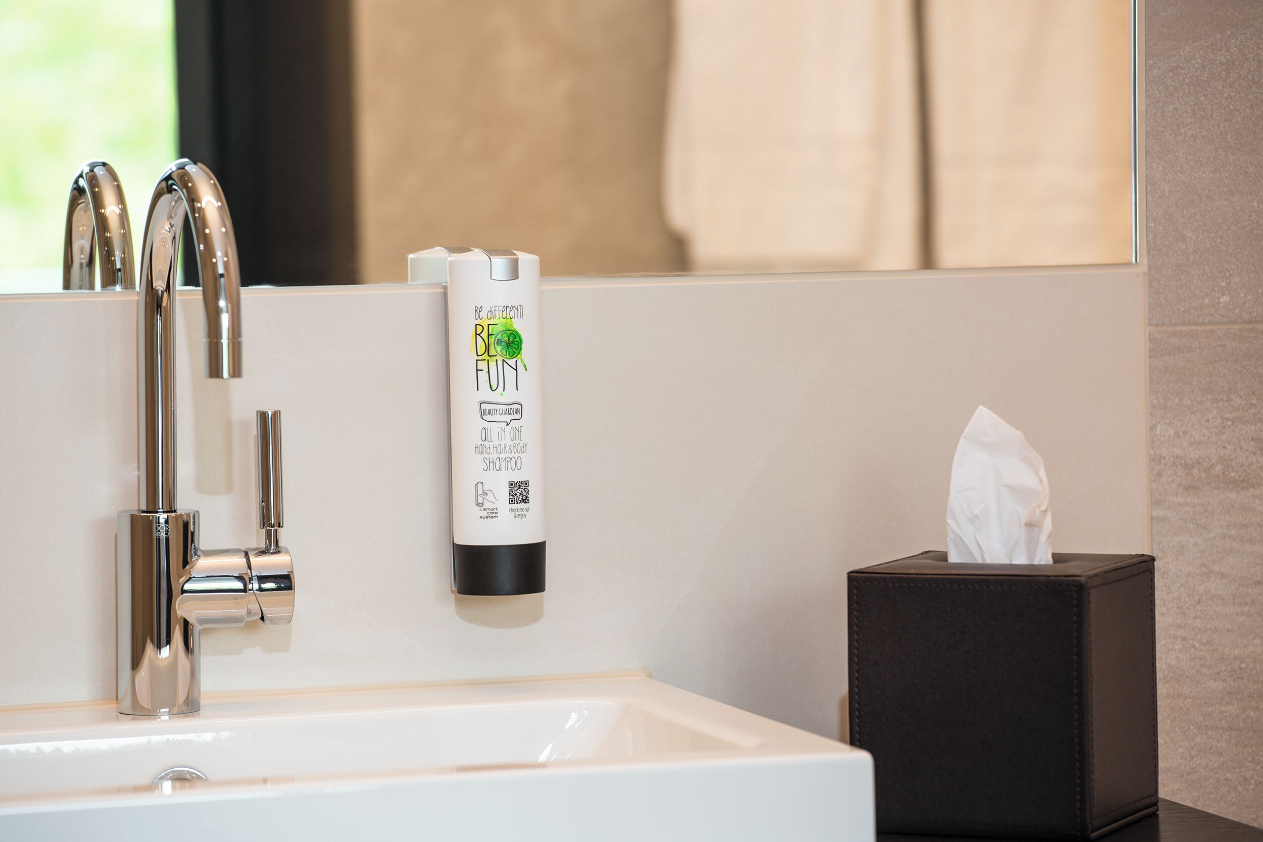 A bathroom with a white sink, chrome faucet, a bottle of shampoo, and a tissue box.