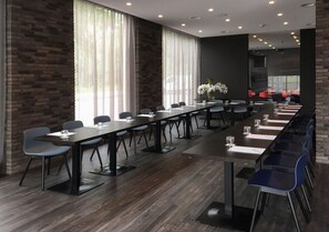 Une salle de conférence avec de longues tables, des chaises et un mur en briques.