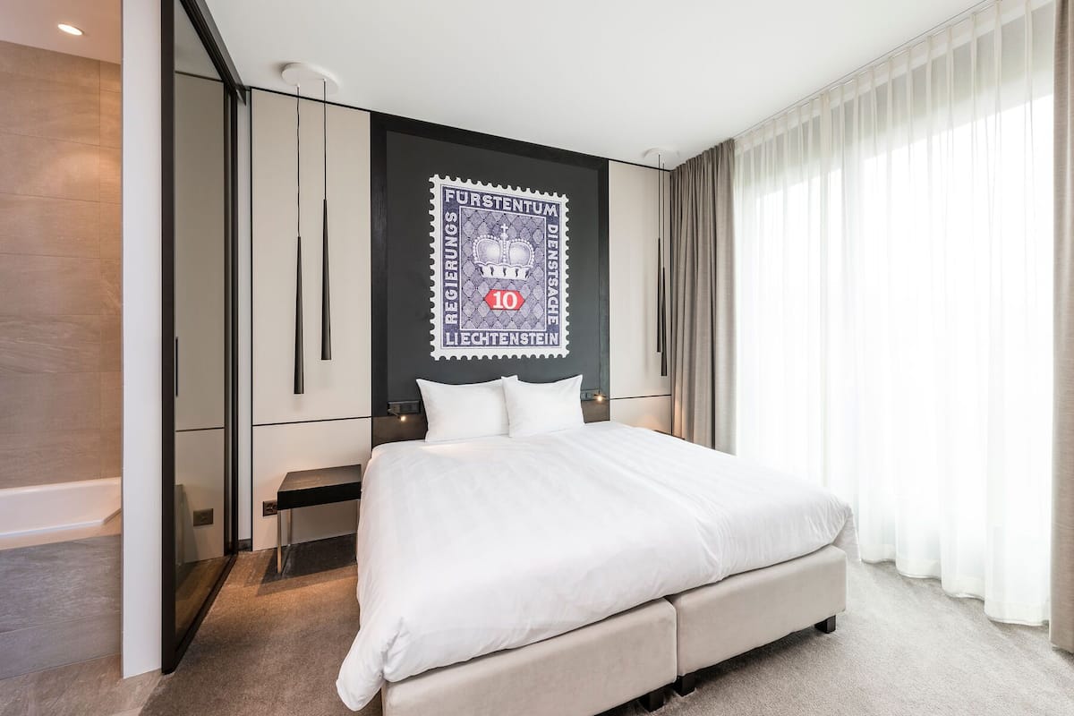A hotel room with a bed, a desk, a wardrobe, and a large window with curtains.