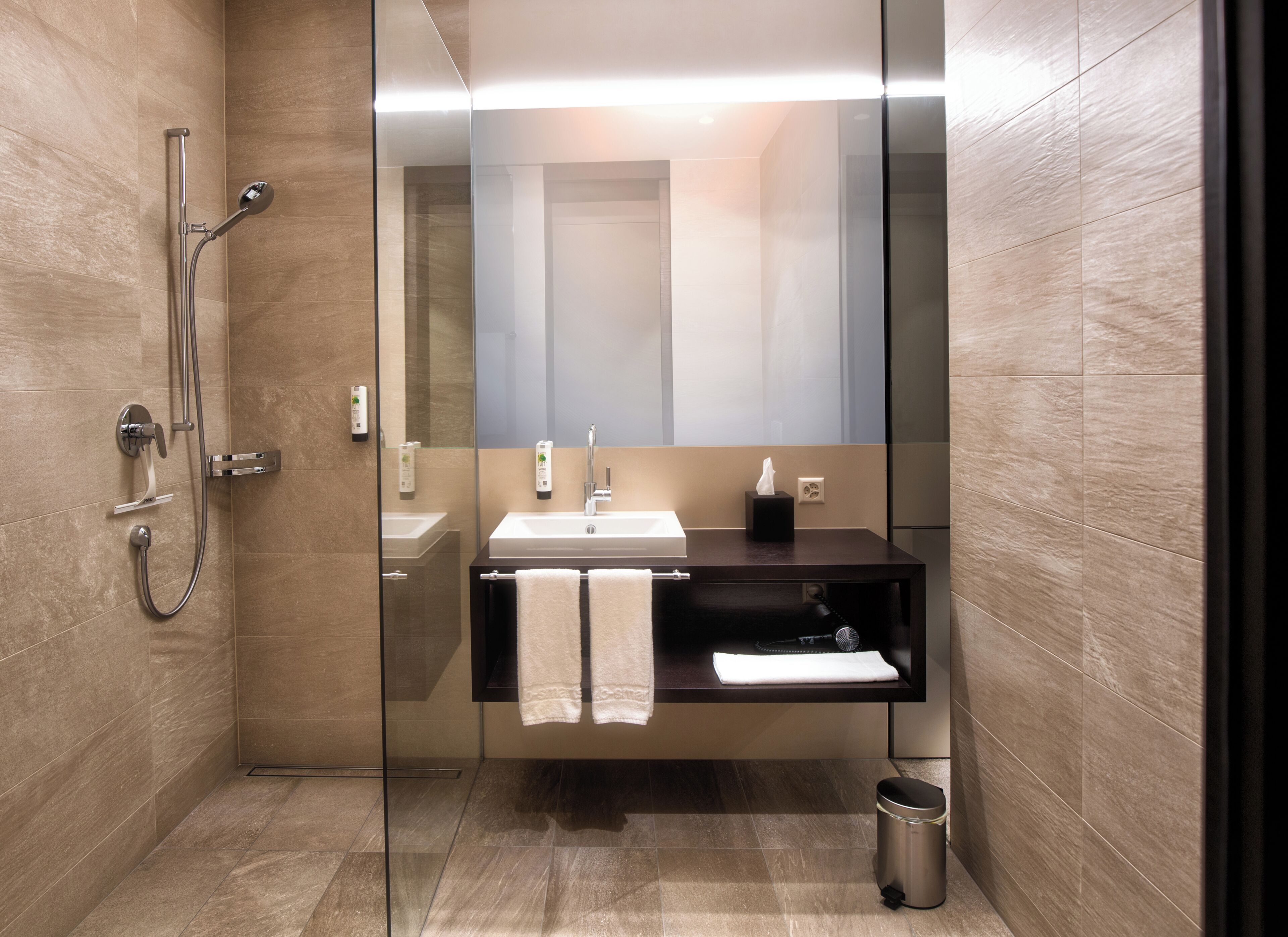 Un bany modern amb plat de dutxa de vidre, un lavabo i un mirall.