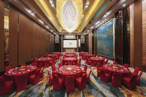 Une salle de conférence équipée de plusieurs tables rondes, de chaises rouges et d’un grand écran situé au fond de la pièce.