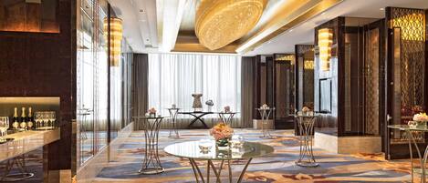 Un moderno vestíbulo de hotel con zona de bar, mesas redondas y un candelabro decorativo.