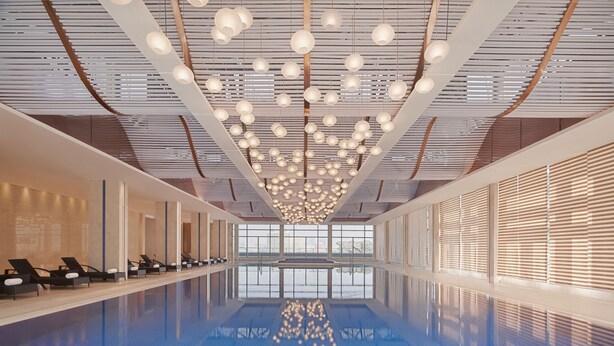 Una piscina interior moderna con suelo azul reflectante, luces en el techo y ventanas iluminadas por el sol.