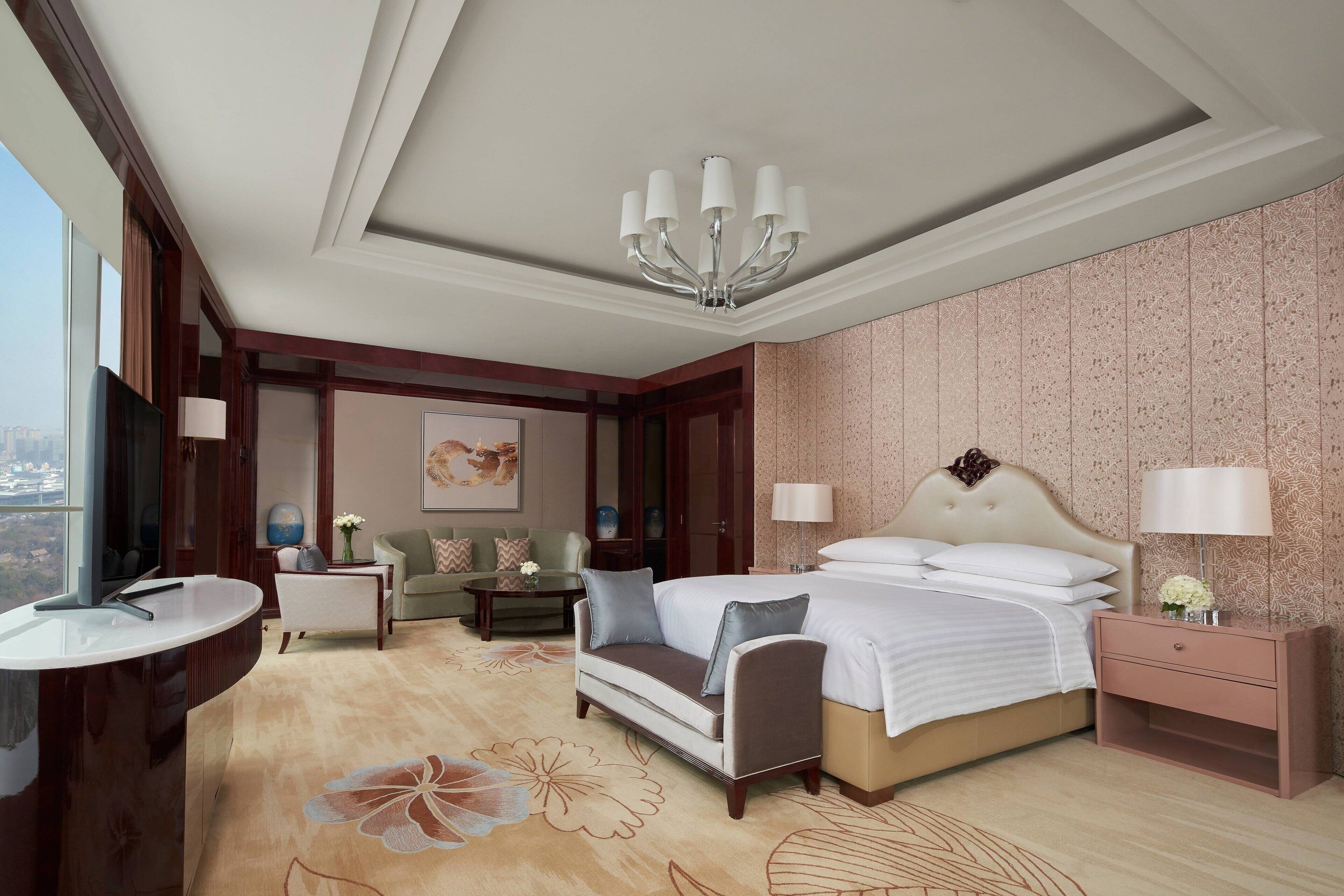 A hotel room with a large bed, bedside tables, a desk, a sofa, and a view of the city.