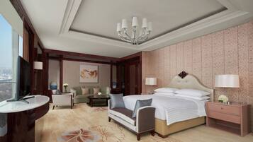 A hotel room with a large bed, bedside tables, a desk, a sofa, and a view of the city.