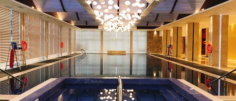 A modern indoor swimming pool with a unique ceiling design, clear water, and a blue tiled floor.