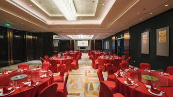 Un salón de conferencias de hotel con mesas redondas, sillas rojas y suelo alfombrado.