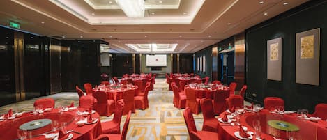 Ein Hotelkonferenzraum mit runden Tischen, roten Stühlen und Teppichboden.
