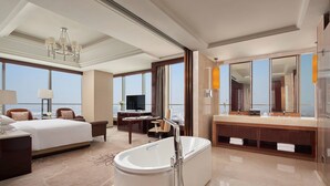 Una habitación de hotel con una cama grande, una zona de estar, una bañera, un tocador con espejo y un televisor.
