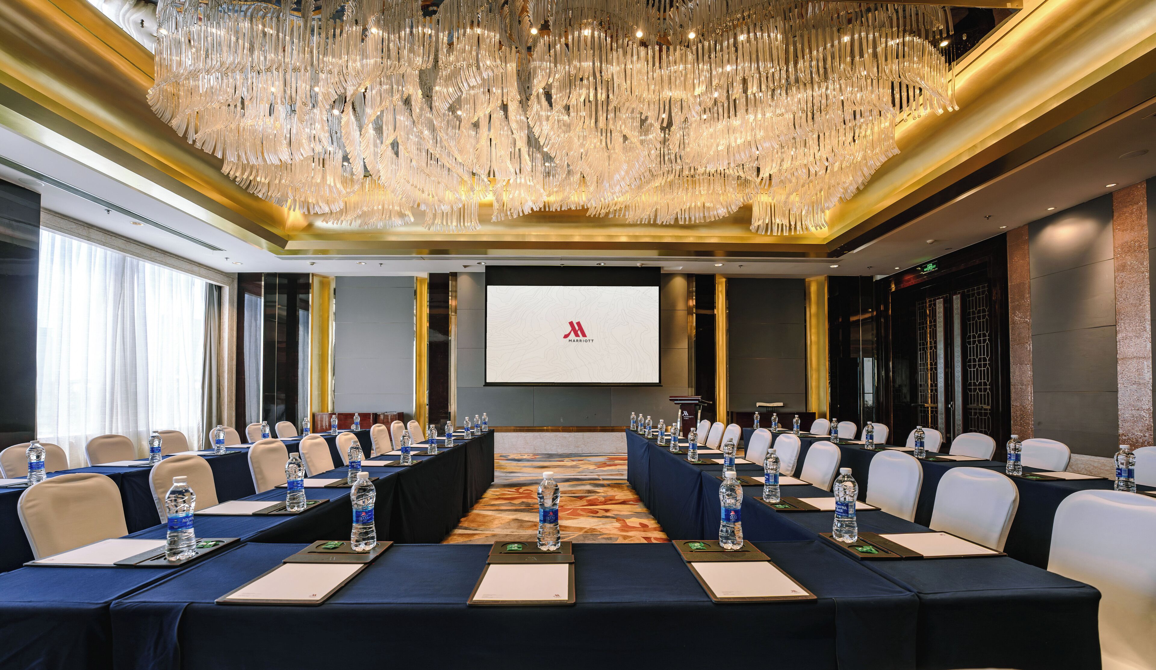 Un salón de conferencias con una larga mesa, botellas de agua y una pantalla de proyector mostrando el logotipo de Marriott.