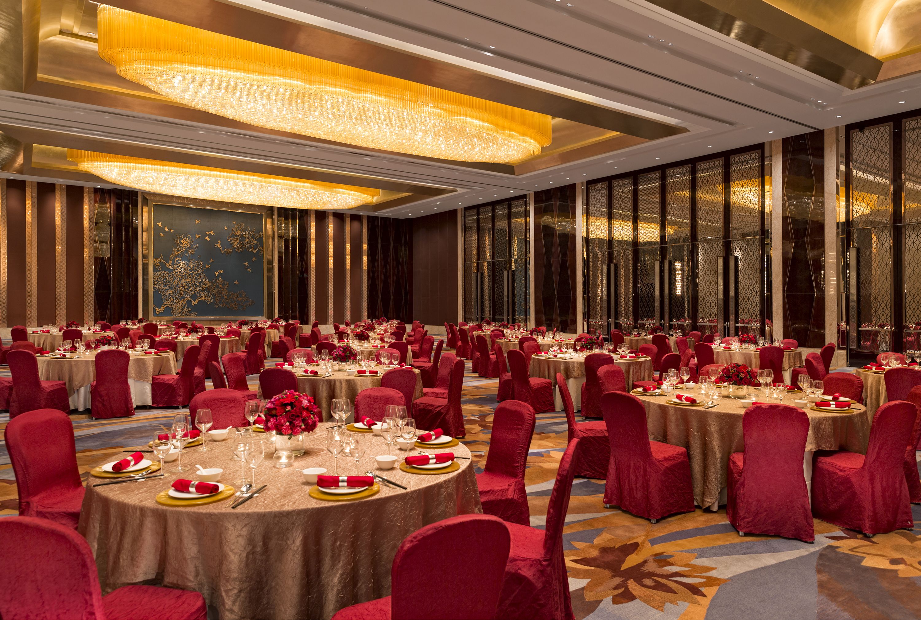 Un salón de banquetes con mesas redondas, sillas rojas y vajilla dorada.