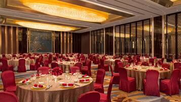 Un salón de banquetes con mesas redondas, sillas rojas y vajilla dorada.