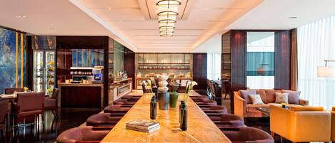A spacious hotel lobby with a long marble reception desk, comfortable seating, and a modern chandelier.