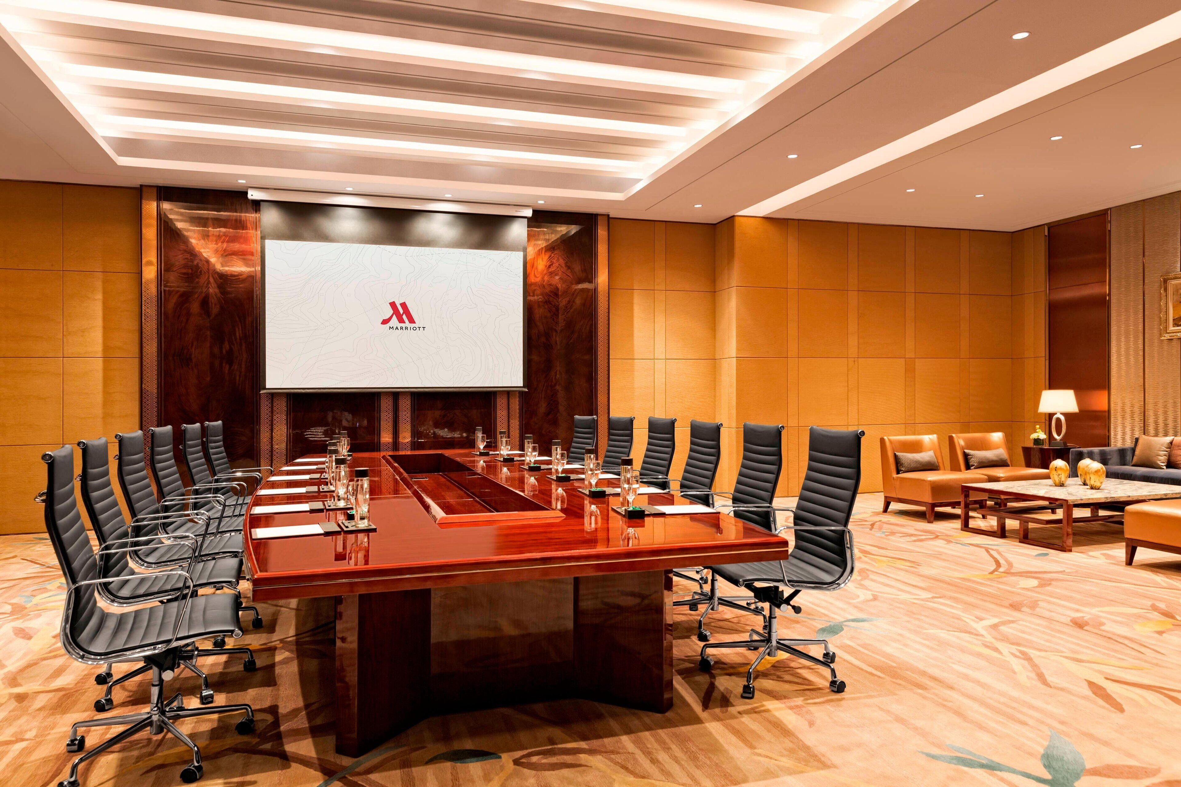 A conference room with a long table, multiple chairs, and a large screen displaying a logo.