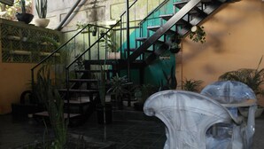 Un escalier avec une rampe en métal, entouré de plantes en pot et de chaises en plastique transparent.