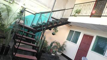 Un edificio de varios niveles con una escalera, plantas en macetas y una puerta roja.