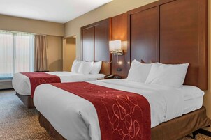 Habitación de hotel con dos camas, una colcha roja y blanca, un cabecero de madera, una mesita de noche y una lámpara.