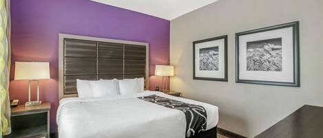 Habitación de hotel con una cama grande, dos mesitas de noche con lámparas, un escritorio y dos cuadros en la pared.