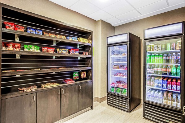 Zona de máquinas expendedoras de aperitivos y bebidas, con estantes llenos de diversos bocadillos y un refrigerador con bebidas embotelladas.