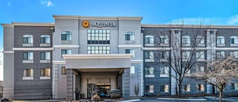 Un moderno edificio de hotel con un llamativo letrero de 'La Quinta', que presenta una fachada simétrica con múltiples ventanas y una entrada central.