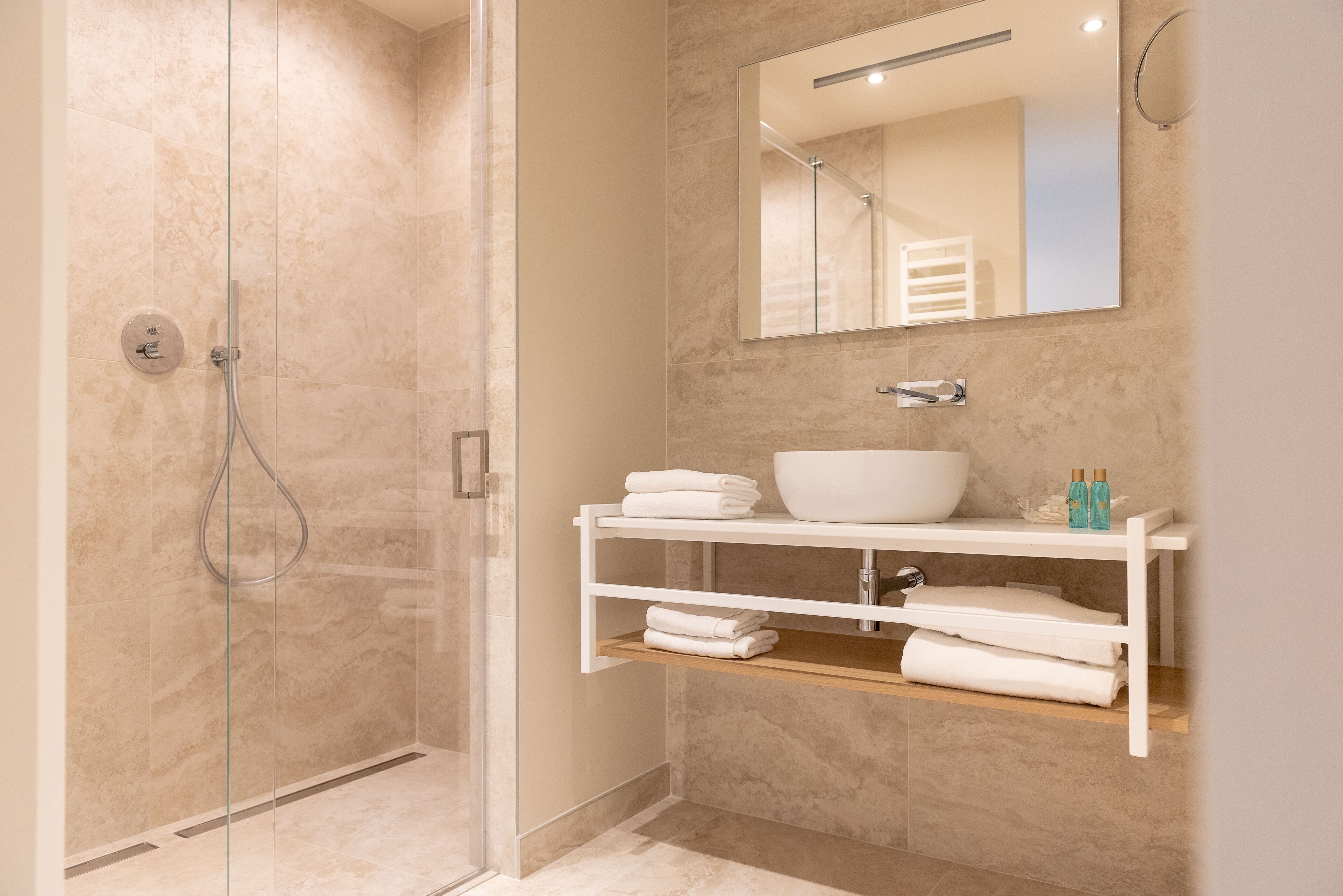Un baño moderno con ducha envuelta en vidrio, un lavamanos blanco y un espejo encima.