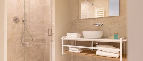 Un baño moderno con ducha envuelta en vidrio, un lavamanos blanco y un espejo encima.