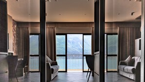 A modern hotel room with a large window offering a mountain view, a herringbone-patterned floor, and a seating area with a sofa and chairs. - Hotel Splendid Palace (Limone sul Garda)