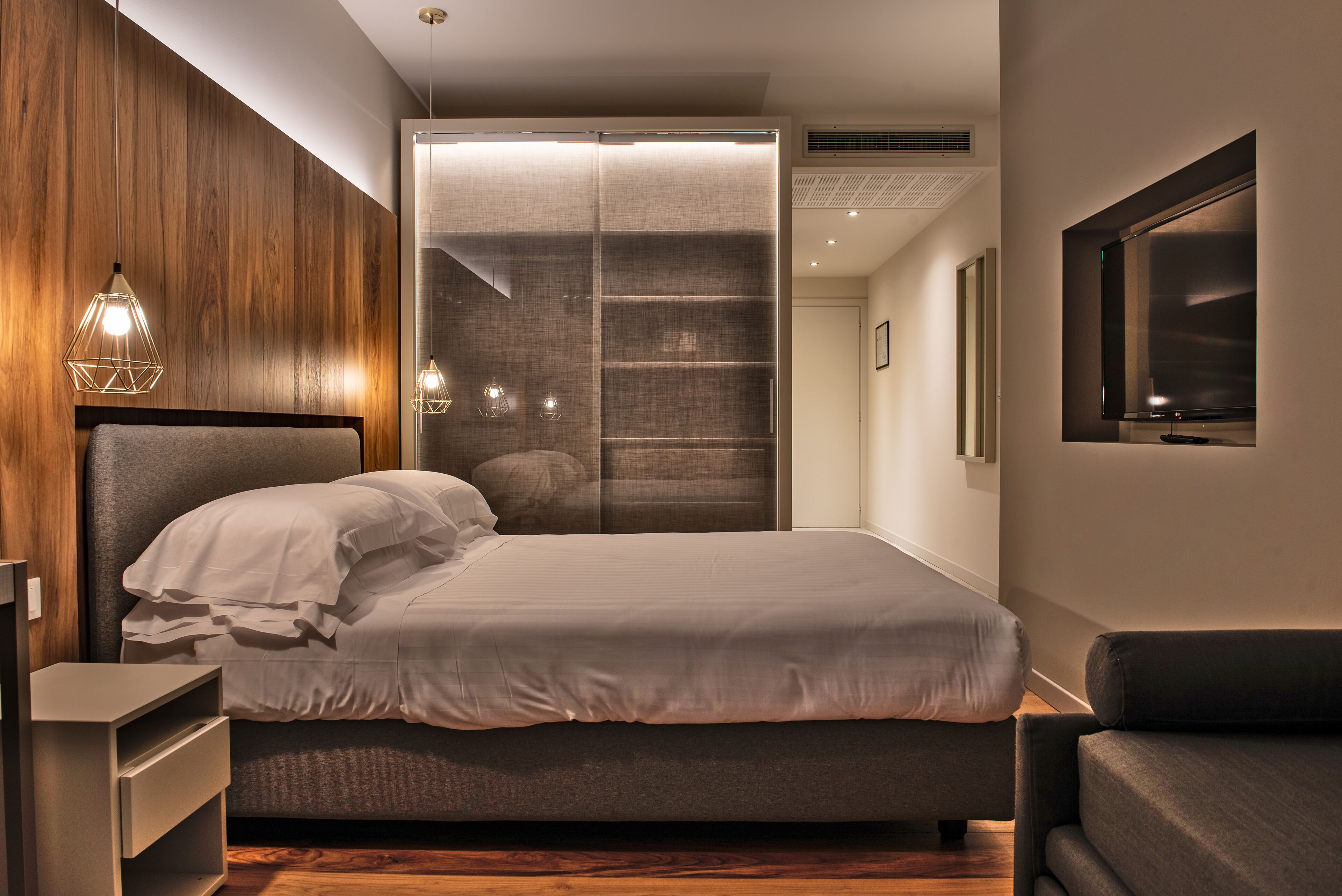 A modern bedroom with a large bed, built-in shelving, and a TV mounted on the wall.
