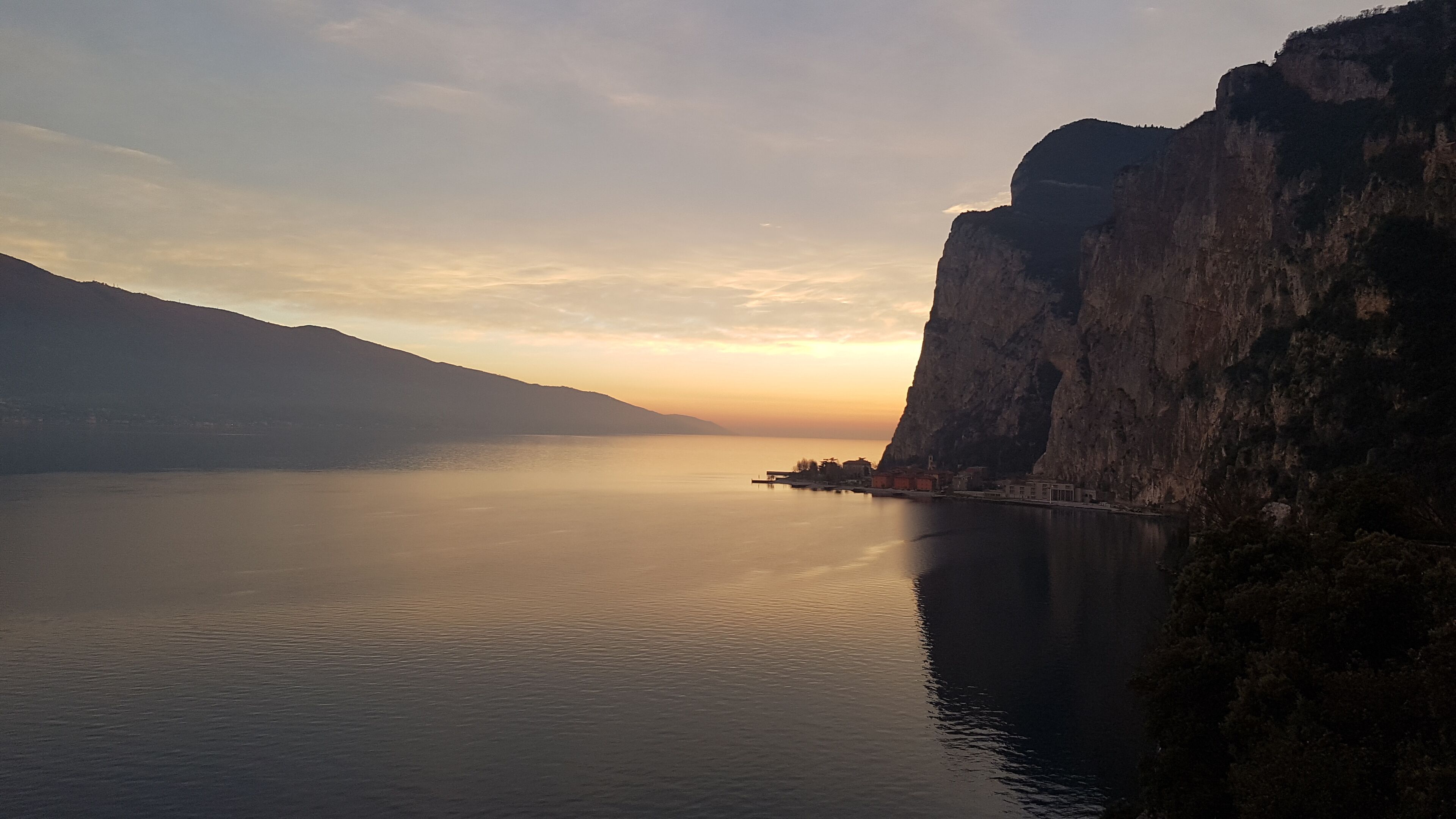 A coastal landscape with a calm sea, a steep cliff, and a small settlement at the base.